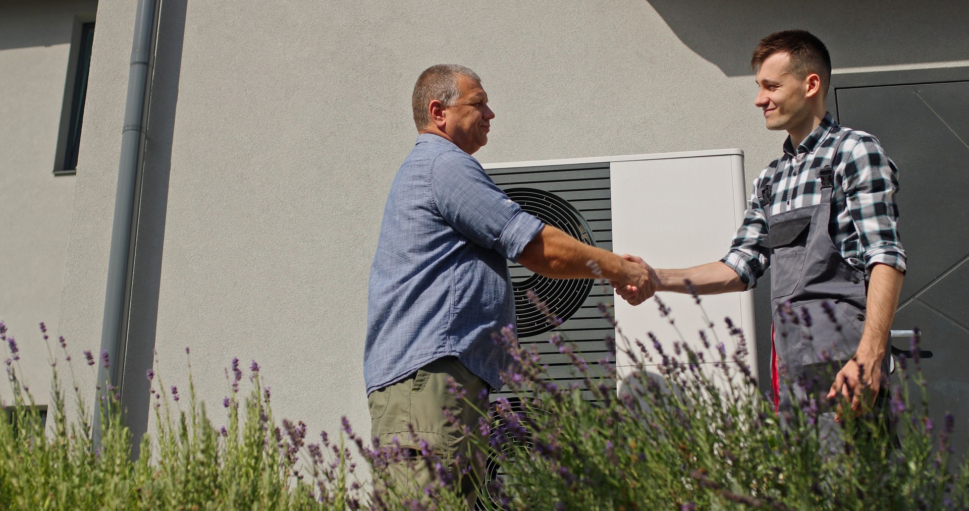 A technician and homeowner finalize their consultation with a handshake beside an external heat pump unit.